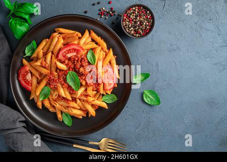 Penne mit Bolognese-Sauce auf Graphituntergrund. Mit Gewürzen und Basilikum. Italienische Küche. Stockfoto