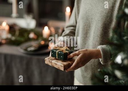 Nahaufnahme einer nicht erkennbaren jungen Frau, die kleine Weihnachtsgeschenke in einem mit Kerzen dekorierten Zimmer hält, Kopierraum Stockfoto