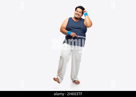 Porträt eines fetten Mannes, der lächelt, während er vor schlichtem Hintergrund ein Maßband um seine Taille wickelt. Stockfoto