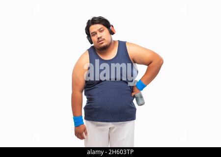 Portait eines fetten Mannes, der nach einem Training erschöpft mit Kopfhörern um den Hals steht. Stockfoto