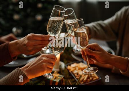 Nahaufnahme von vier Personen, die gemeinsam ein Weihnachtsessen genießen und mit Sektgläsern toasten, während sie am eleganten Esstisch mit Kerzen sitzen Stockfoto