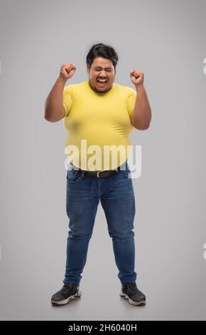 Porträt eines fetten Mannes, der vor schlichtem Hintergrund mit den Fäusten feiert. Stockfoto