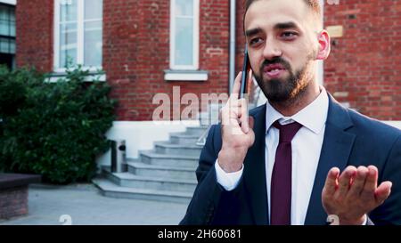 Porträt eines Geschäftsmannes in diplomatischem Anzug, der vor dem Büro eines Start-ups steht und am Telefon über die Finanzstrategie mit einem Remote-Manager spricht. Outdoor-Konzept Stockfoto