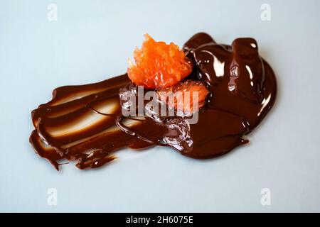 Aufgelöste Bitterschokolade, die auf Glasplatte mit Stücken süßer roter Grapefruit verschüttet wurde, Nahaufnahme. Stockfoto