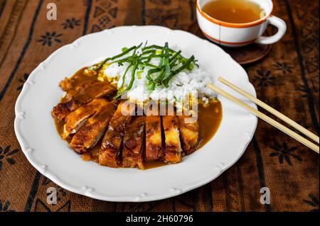 In Scheiben geschnittenes Hühnerfleisch, gebraten in knuspriger Panko-Brotkrume mit geschmortem Reis und würziger, scharfer Sauce, Essstäbchen, einer Tasse Tee. Asiatisches Essen. Stockfoto