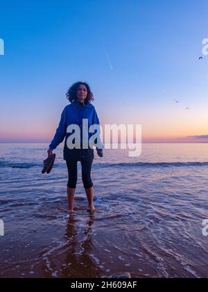 Frauen paddeln im Meer bei Sonnenuntergang mit Sternen, Mond und Flugzeug-Trails dahinter Stockfoto