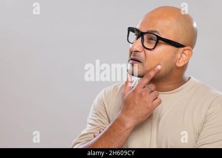 Porträt eines kahlen Mannes, der mit den Händen am Kinn vor schlichtem Hintergrund denkt. Stockfoto