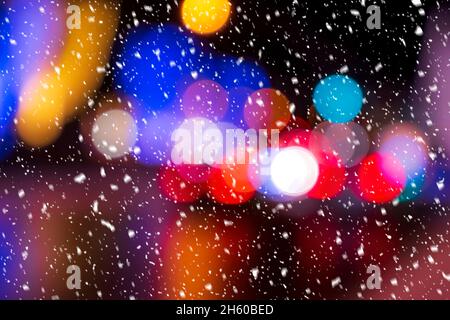 Verschwommenes Licht von Scheinwerfern von Autos und Laternen in der Nachtstadt bei Schneefall. Abstraktes helles Bokeh. Stockfoto