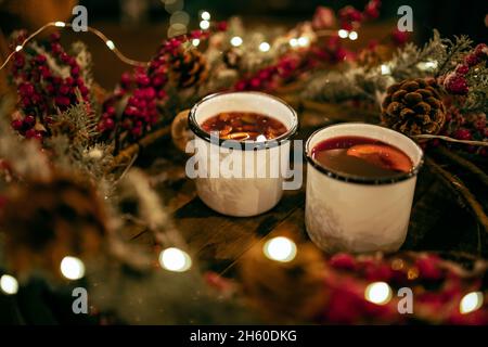 Zwei Tassen Winter Glühwein mit Gewürzen und Orangenscheiben auf Holztisch mit weihnachtlichen Dekorationen. Stillleben mit traditionellem Getränk Stockfoto