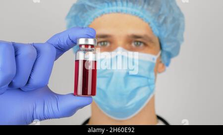 Der Arzt füllt eine Spritze mit einem roten Impfstoff und bereitet sich darauf vor, einen Patienten zu injizieren 19 Stockfoto
