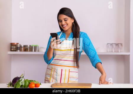 Schöne indische Frau beobachten Smartphone in der Küche Stockfoto