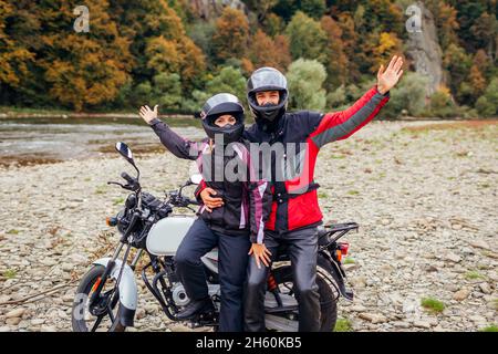 Ein paar Biker fahren im Herbst mit dem Motorrad. Motorradfahrer genießen die herbstliche Landschaft in den Bergen und ruhen sich durch Wald und Fluss aus. Glücklicher Mann und Frau r Stockfoto