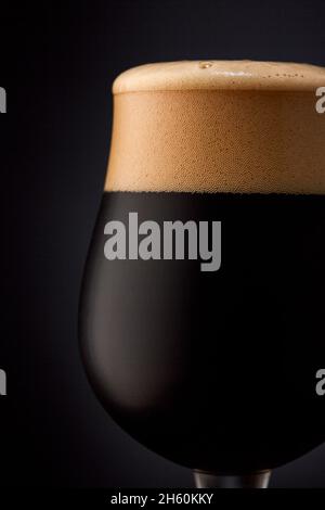 Nahaufnahme eines Glases dunklem Bier auf schwarzem Hintergrund. Stockfoto