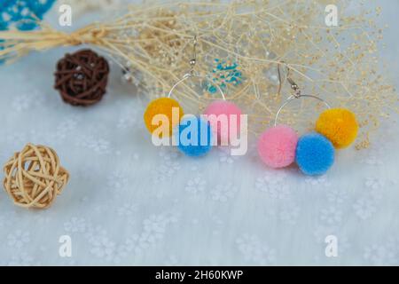 Farbige Pompon-Ohrringe in Form von drei pelzigen Kugeln.Ohrringe sind neben Rattan-Produkten, Blumenmuscheln und anderen Ornamenten Stockfoto