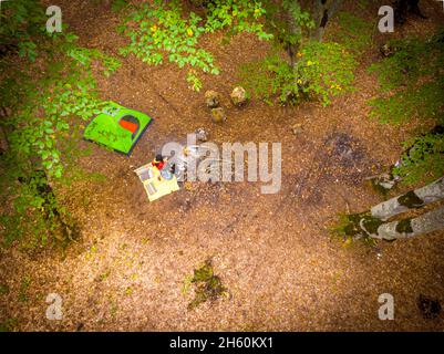 Die Frau sitzt mit dem Jungen am Feuer und in der Nähe befindet sich ein grünes Zelt, umgeben von Bäumen. Luftaufnahme nach unten mit leerem Raum. Stockfoto
