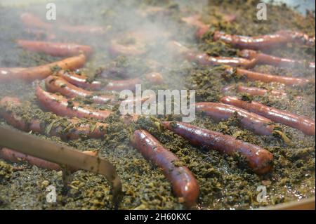 Dampfender Grünkohl oder lockiges Blattkohl in einem großen Topf mit vielen geräucherten Würstchen, traditionelles Winteressen auf einem Herbst- oder Weihnachtsmarkt in Germ Stockfoto