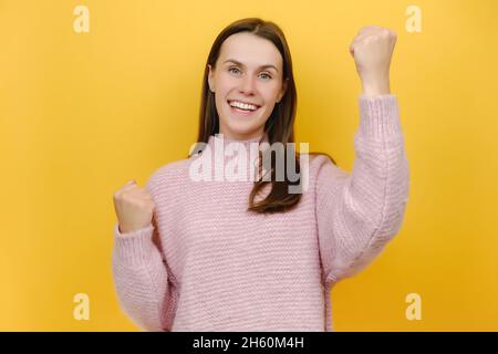 Glücklich aufgeregt erfolgreich überglücklich glücklich attraktiv hübsche junge Frau 20s tun Gewinnergesten Gestus klatschen Fäuste feiern, gekleidet in Strickpullover Stockfoto