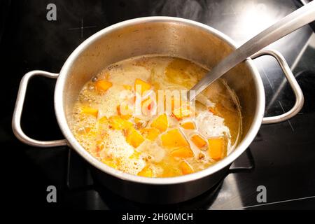 Kochen einer vegetarischen Kürbissuppe aus Hokkaido oder Red kuri Squash in einem Stahltopf auf einem schwarzen Herd, Gemüseherbstgericht, ausgewählter Fokus enge Tiefe Stockfoto