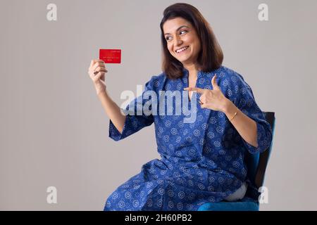 Indische Frau zeigt ihre Kreditkarte, während sie auf einem Stuhl sitzt Stockfoto