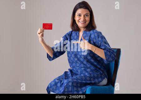 Indische Frau zeigt ihre Kreditkarte, während sie auf einem Stuhl sitzt Stockfoto