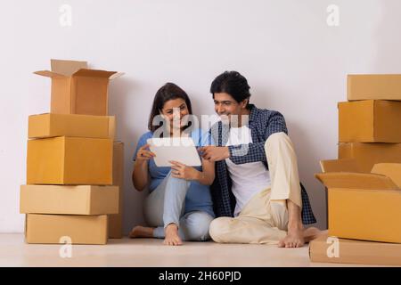 Indisches Paar mittleren Alters beobachten Tablet zusammen in neuem Zuhause Stockfoto