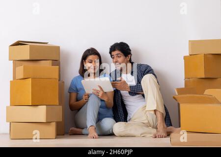 Indisches Paar mittleren Alters beobachten Tablet zusammen in neuem Zuhause Stockfoto