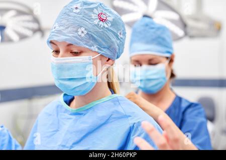 Die chirurgische Krankenschwester hilft der Ärztin, sich vor einer Operation Schutzkleidung zu tragen Stockfoto