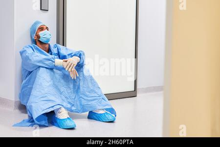 Erschöpfter Chirurg oder Krankenschwester macht wegen Covid-19 eine Pause vor der Intensivstation Stockfoto