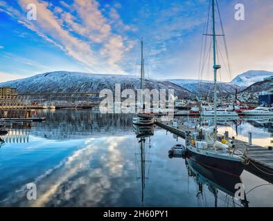 Blick über den Hafen in Tromso in Richtung Tromsdalen, vor dessen Hintergrund die Tromso-Brücke und die ikonische arktische Kathedrale stehen. Stockfoto