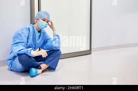 Krankenschwester oder Krankenschwester sitzt müde und nachdenklich vor der Intensivstation der Klinik Stockfoto