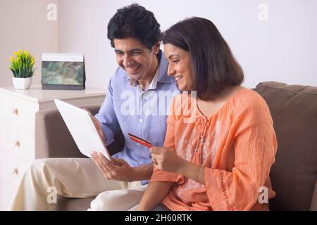 Indisches Ehepaar mittleren Alters online über Tablet mit Kreditkarte einkaufen Stockfoto