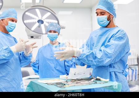 Chirurgen in Schutzkleidung und mit Gesichtsmasken ziehen vor der Operation Einweghandschuhe an Stockfoto