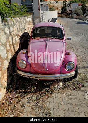 Verlassene rosa Volkswagen Beetle Auto auf der Straße in der Nähe der Steinmauer geparkt. Stockfoto