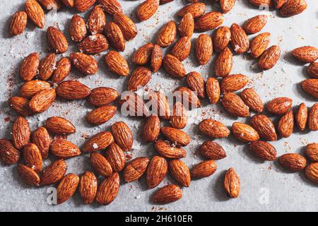 Rohe Mandeln, die mit Olivenöl, Meersalz und geräuchertem Paprika auf einem Backblech zubereitet werden, das zum Rösten bereit ist. Stockfoto