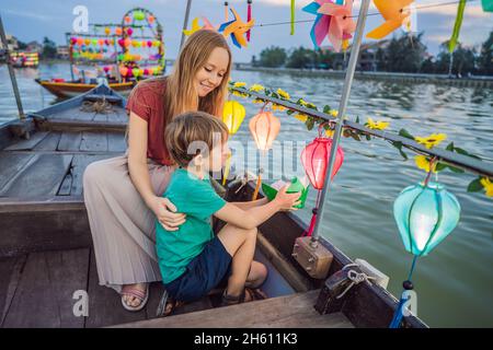 Glückliche Familie Mutter und Sohn von Reisenden reiten auf einem Nationalboot auf dem Hintergrund der alten Stadt Hoi, Vietnam. Vietnam öffnet sich danach wieder für Touristen Stockfoto