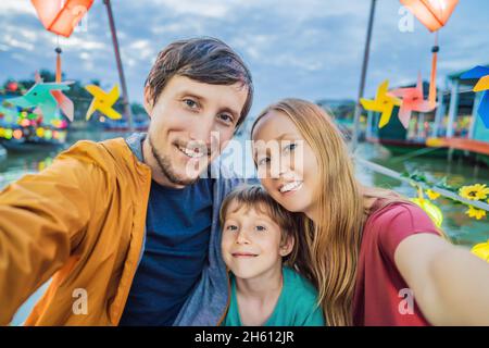 Glückliche Familie von Reisenden fahren ein nationales Boot auf dem Hintergrund der Hoi an alten Stadt, Vietnam. Vietnam öffnet sich nach der Quarantäne wieder für Touristen Stockfoto