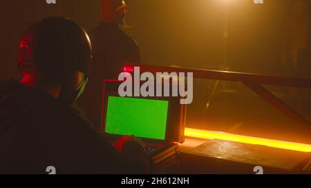 Schießsaal mit Schauspielern vor der Kamera. Archivmaterial. Der Mann im Helm sitzt auf dem Laptop mit einem grünen Bildschirm vor dem Hintergrund der Schauspieler, die vor der Kamera stehen Stockfoto