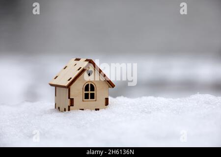 Hölzernes Hausmodell auf dem Schnee. Konzept von Landhaus, Wohnungssuche im Winter, Immobilien in ökologisch sauberer Umgebung Stockfoto