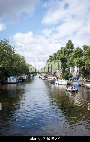 Ein kleines Motorboot fährt mit Hausbooten entlang eines Kanals im Zentrum von Amsterdam, Niederlande. Da 50 % der Niederlande unter dem Meeresspiegel liegen, ist sie unglaublich anfällig für den durch den Klimawandel angetriebenen Anstieg des Meeresspiegels. Sie schränkt auch die Menge an bewohnbarem Platz für Menschen ein und es müssen alternative Lösungen gefunden werden. Stockfoto