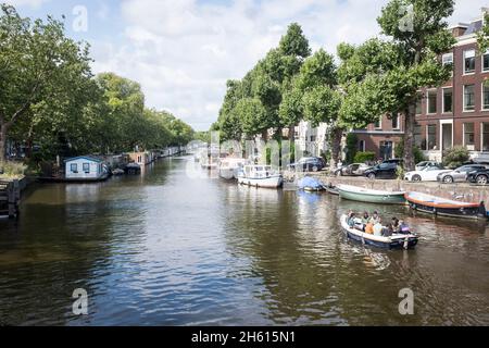 Ein kleines Boot fährt an Hausbooten vorbei, die an einem Kanal im Zentrum von Amsterdam, Niederlande, festgemacht sind. Da 50 % der Niederlande unter dem Meeresspiegel liegen, ist sie unglaublich anfällig für den durch den Klimawandel angetriebenen Anstieg des Meeresspiegels. Sie schränkt auch die Menge an bewohnbarem Platz für Menschen ein und es müssen alternative Lösungen gefunden werden. Stockfoto