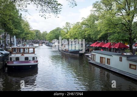 Viele Hausboote liegen an einem Kanal im Zentrum von Amsterdam, Niederlande. Da 50 % der Niederlande unter dem Meeresspiegel liegen, ist sie unglaublich anfällig für den durch den Klimawandel angetriebenen Anstieg des Meeresspiegels. Sie schränkt auch die Menge an bewohnbarem Platz für Menschen ein und es müssen alternative Lösungen gefunden werden. Stockfoto