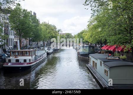 Hausboote vertäuten Nase an Schwanz entlang eines Kanals im Zentrum von Amsterdam, Niederlande. Da 50 % der Niederlande unter dem Meeresspiegel liegen, ist sie unglaublich anfällig für den durch den Klimawandel angetriebenen Anstieg des Meeresspiegels. Sie schränkt auch die Menge an bewohnbarem Platz für Menschen ein und es müssen alternative Lösungen gefunden werden. Stockfoto