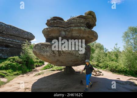 Wanderfrau, Blick auf eine reife Wanderin, die am Idol Rock, einer dramatischen Felsformation in Brimham Rocks, North Yorkshire National Park, England, spazieren geht Stockfoto