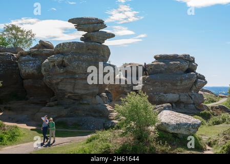 Brimham Rocks, Blick im Sommer auf ein Seniorenpaar, das an einer stark erodierten Felsformation bei Brimham Rocks in Nidderdale, North Yorkshire, England, vorbeigeht Stockfoto