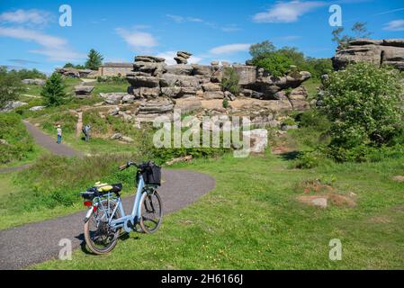 Radfahren, Blick im Sommer auf ein Seniorenpaar, das Brimham Rocks in North Yorkshire mit einem blauen Vintage-Fahrrad erkundet, das im Vordergrund, England, Großbritannien, geparkt ist Stockfoto