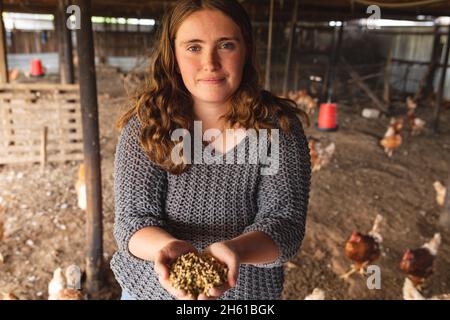 Porträt einer schönen jungen Gehöft-Hündin mit Körnerpellets in kuppeligen Händen in Hühnerstall Stockfoto