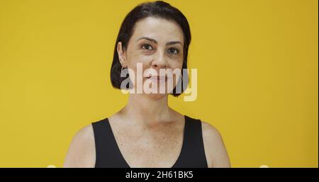 Attraktive Frau mittleren Alters mit einem schönen Lächeln auf der gelben Wand. Ziemlich ältere Frau, erfolgreiches Vertrauen. Stockfoto