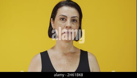 Attraktive Frau mittleren Alters mit einem schönen Lächeln auf der gelben Wand. Ziemlich ältere Frau, erfolgreiches Vertrauen. Stockfoto