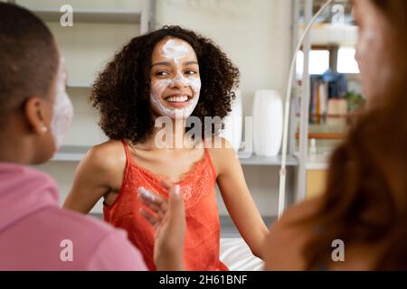 Glückliche biracial Freundinnen mit Gesichtsmasken verbringen Freizeit zu Hause am Wochenende Stockfoto