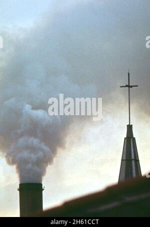 Der Rauchschornstein der Kaiser-Aluminium-Fabrik, hinter der katholischen Kirche, schellt Dämpfe über dem Wohngebiet im Chalmette-Teil von New Orleans Ca. März 1973 Stockfoto